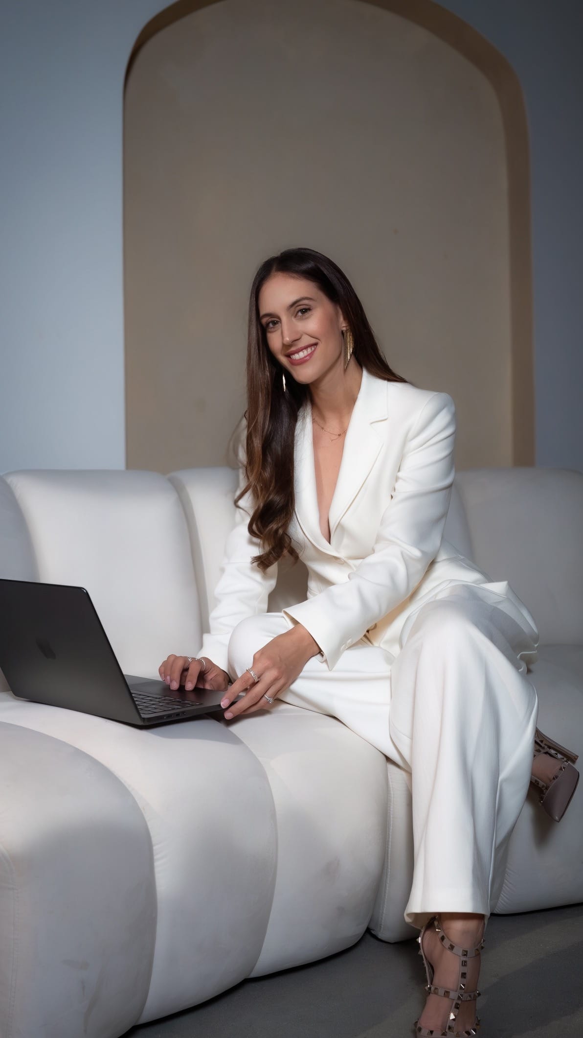 Veronica Lopez-Calleja, Esq., smiling at her laptop in a white suit